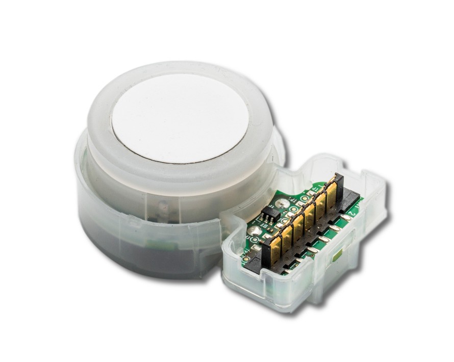 Rund elektronisk sensor med vitt lock och synliga guldfärgade kontaktstift på ett grönt kretskort.