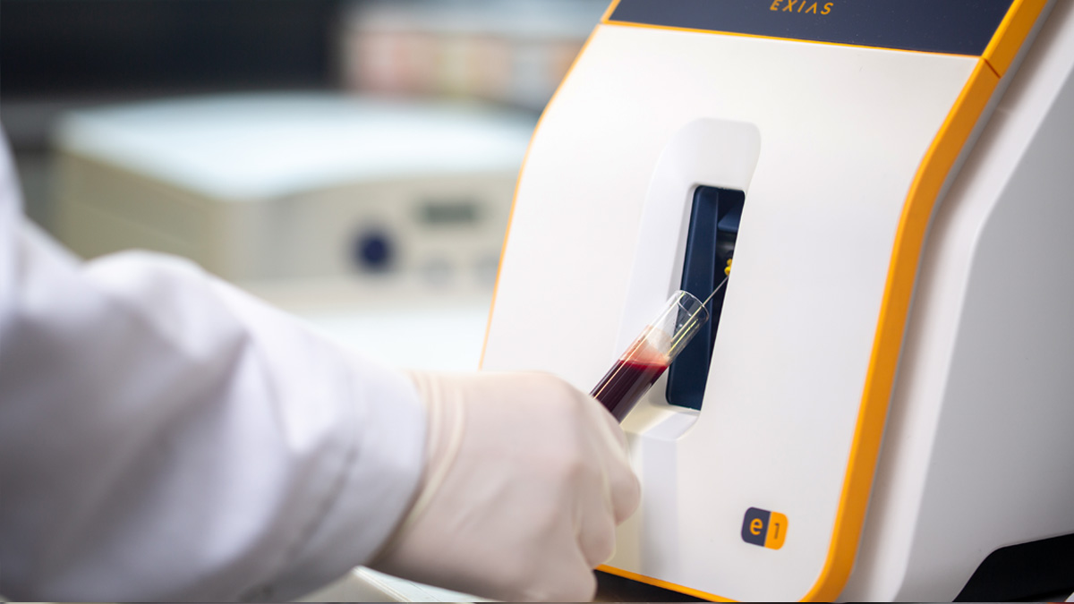 Hansket hånd som setter et blodprøverør inn i et laboratorieanalyseapparat.