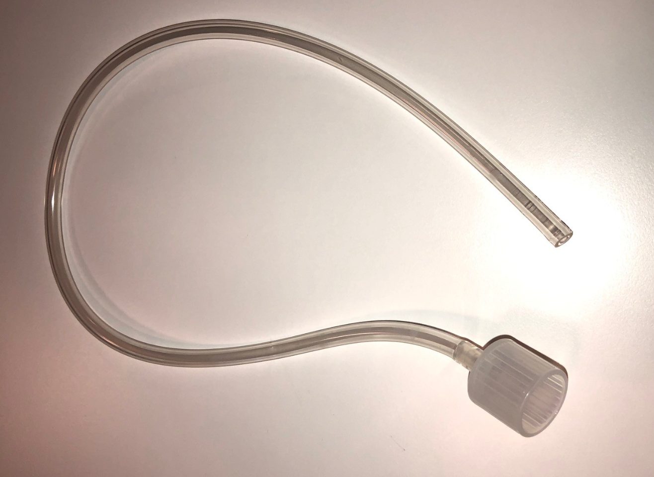 Ett genomskinligt plast rör med ett räfflat lock i ena änden, hoprullat på en vit yta.