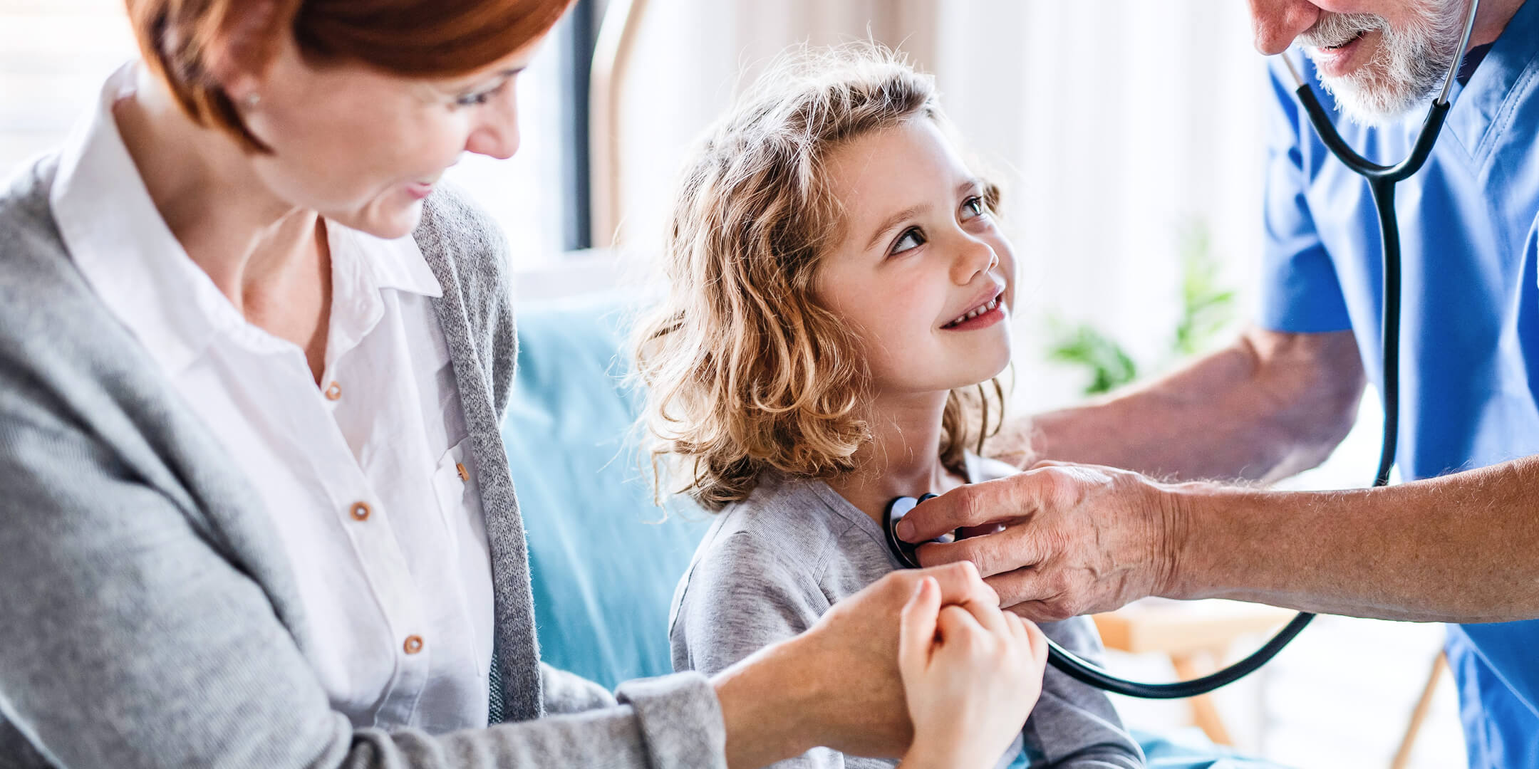Ung jente som sitter på morens fang under en legekonsultasjon og smiler