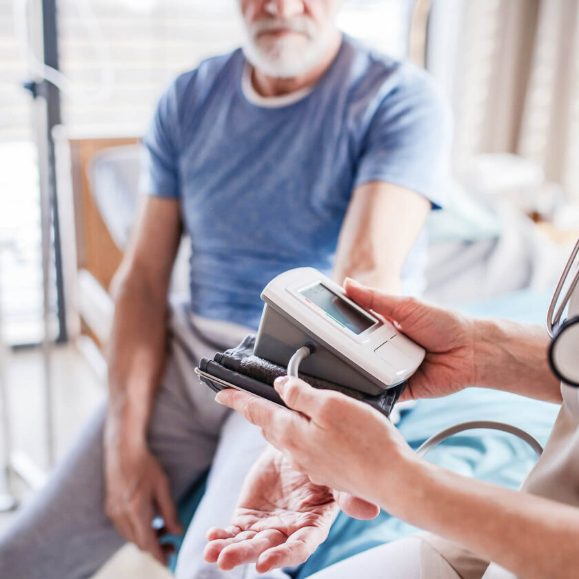 Eldre mann får målt blodtrykket sitt av helsepersonell med digitalt blodtrykksapparat.