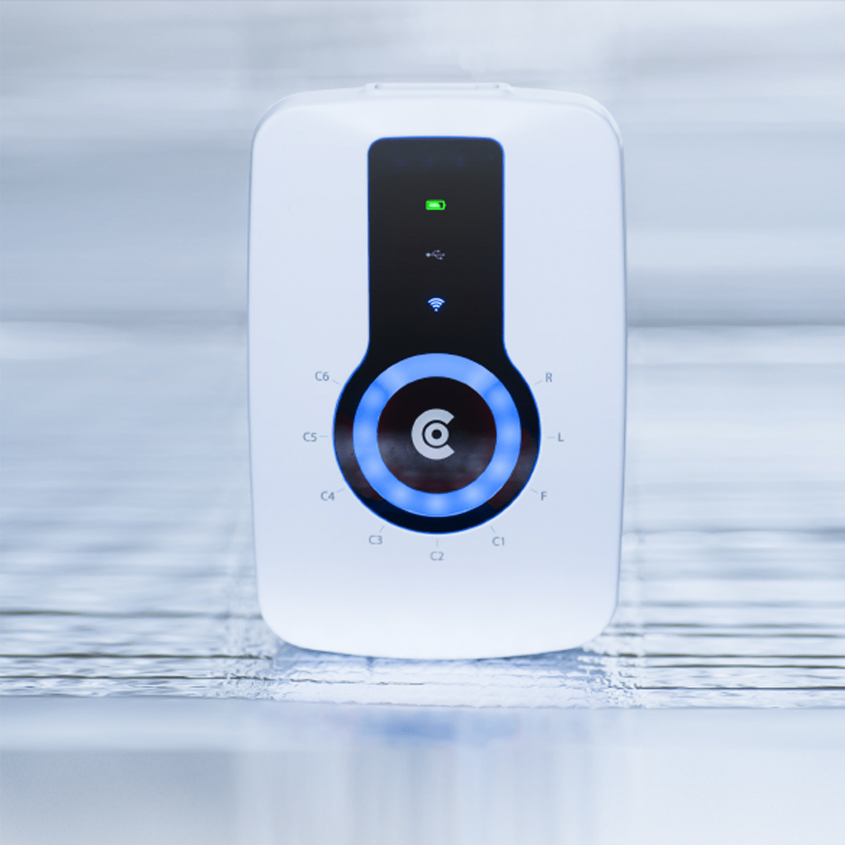 Vitt elektroniskt enhet med en cirkulär blå LED-indikator och svart panel, stående på en reflekterande yta.