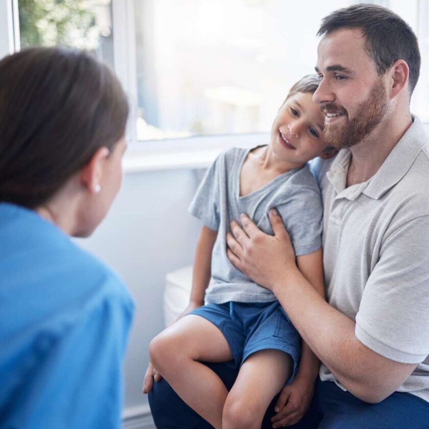 Lege som konsulterer en ung gutt som sitter på fanget til faren sin på et sykehus