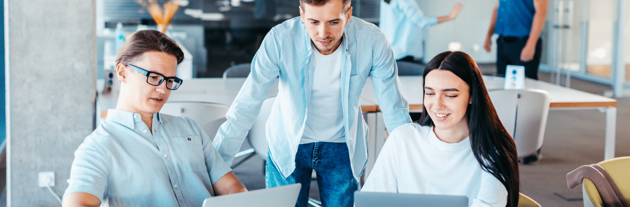 Tre unge fagpersoner som samarbeider på bærbare datamaskiner i et moderne kontorlokale.