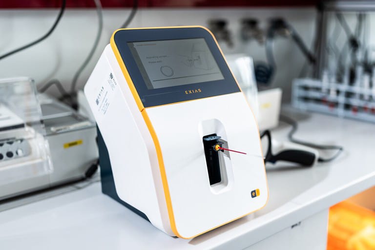 Medisinsk analyseenhet med en skjerm og en prøveholder i et laboratoriemiljø.