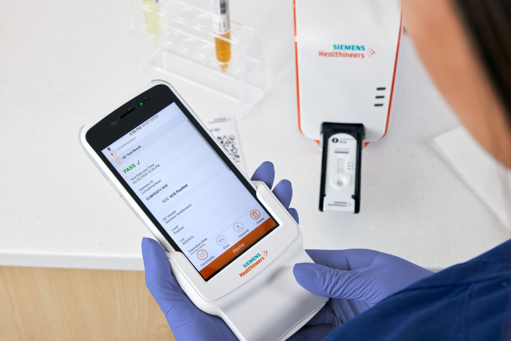 Hanskerte hender holder en Siemens Healthineers diagnostisk enhet som viser et testresultat i et medisinsk laboratoriemiljø.